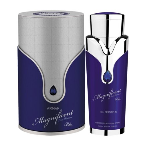 Fioletowy flakon perfum z metalicznymi akcentami i niebieskim kryształem na środku, obok cylindrycznego opakowania w podobnej kolorystyce. Na flakonie widoczny jest napis: "Magnificent Pour Homme Blu Eau de Parfum 100 ml".
