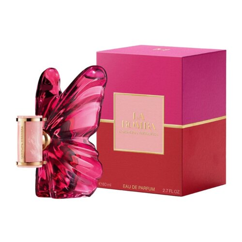 Flakon perfum w kształcie motyla w kolorze różowym znajduje się obok różowo-czerwonego pudełka z napisem "LA BOMBA CAROLINA HERRERA". Na dole pudełka widnieje napis "Eau de Parfum 80 ml 2.7 FL OZ".