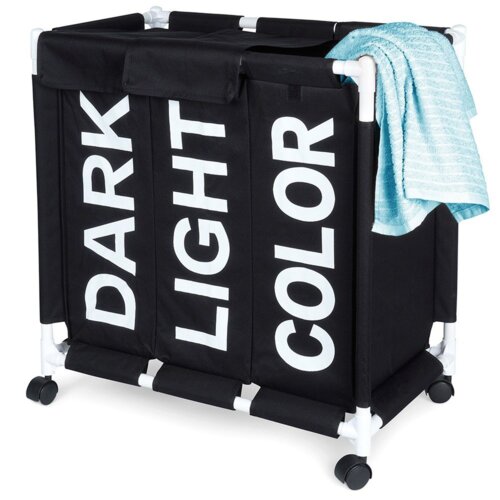 Czarny, trzykomorowy kosz na pranie na kółkach z białymi napisami "DARK", "LIGHT" i "COLOR" na każdej z komór, z niebieskim ręcznikiem przewieszonym przez bok. Konstrukcja kosza jest wsparta na białych rurkach i czarnych kółkach.